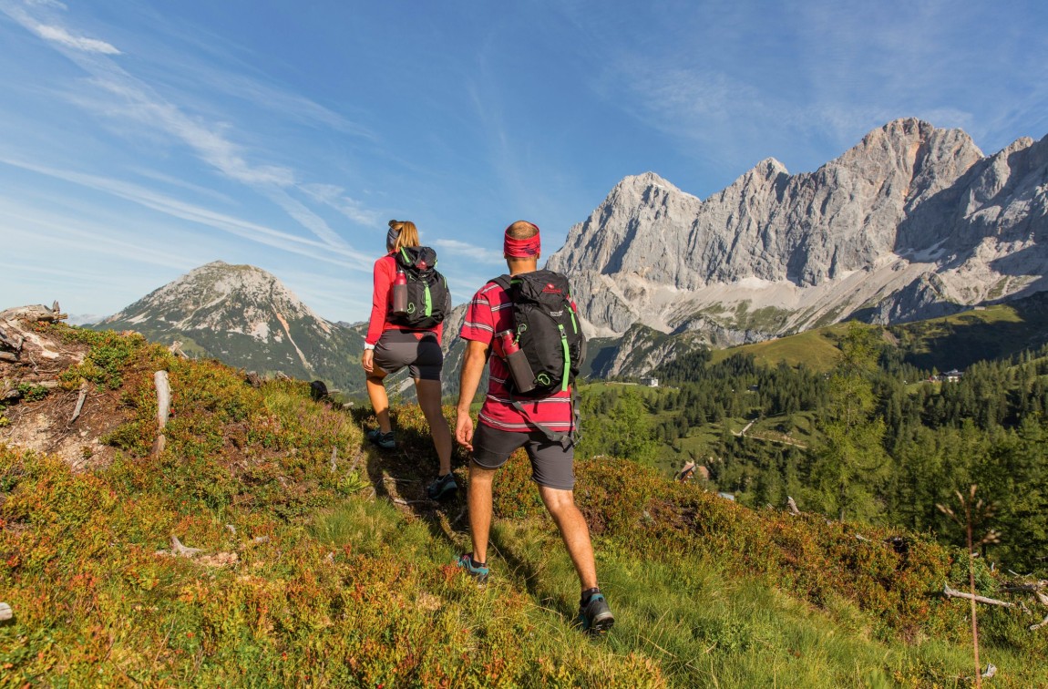 Two hikers with rucksacks from Hotel Lindenhof look at the mountain landscape of Ramsau am Dachstein