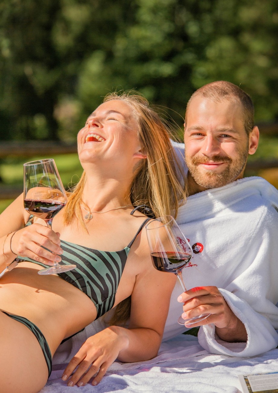  Couple relaxing by the pool with wine at the Hotel Lindenhof in the sunshine