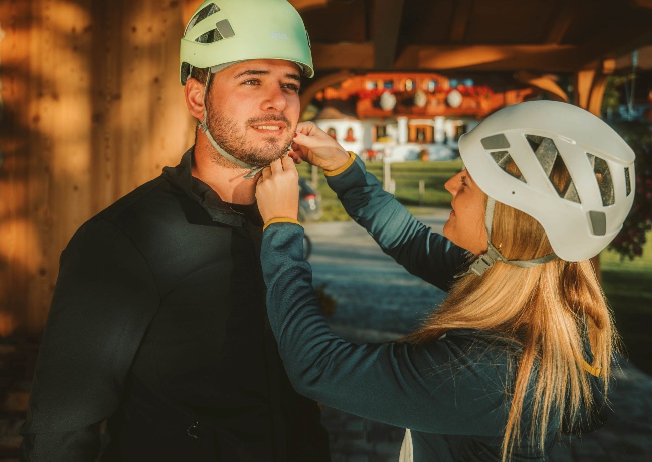 Mann wird von einer Frau beim Anpassen eines Kletterhelms unterstützt