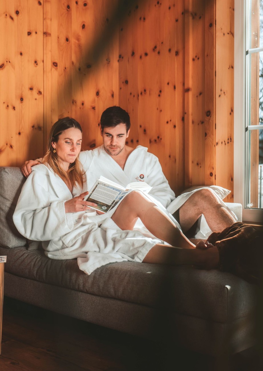 Paar in Bademänteln, entspannt lesend im Wellnessbereich