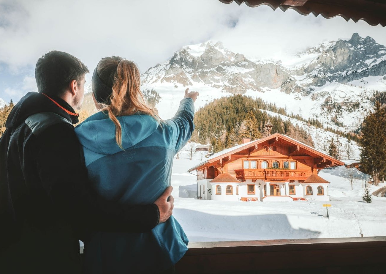 Paar blickt von einem Balkon auf die verschneite Berglandschaft