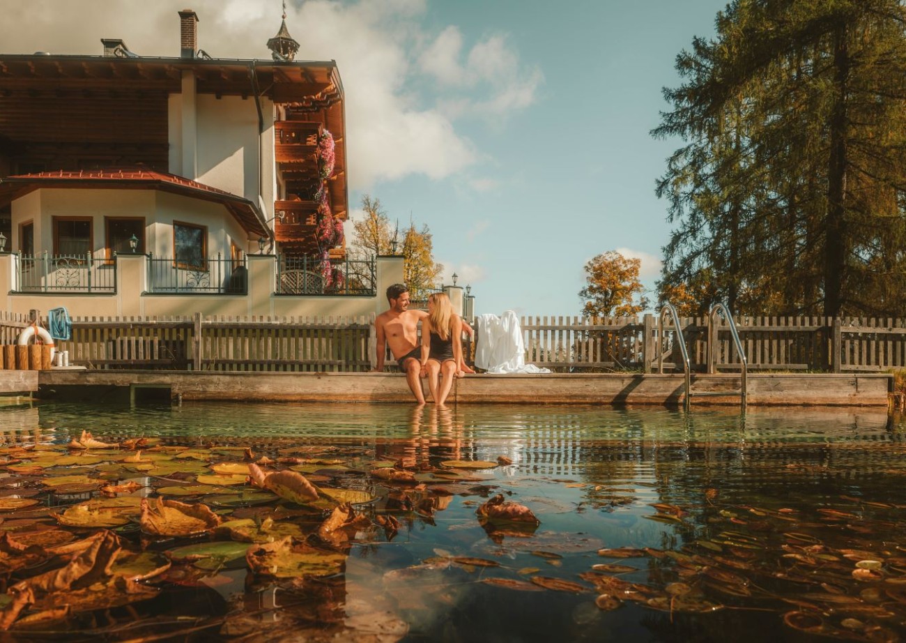 Couple enjoying the relaxing atmosphere by the natural pond at Hotel Lindenhof in Ramsau am Dachstein